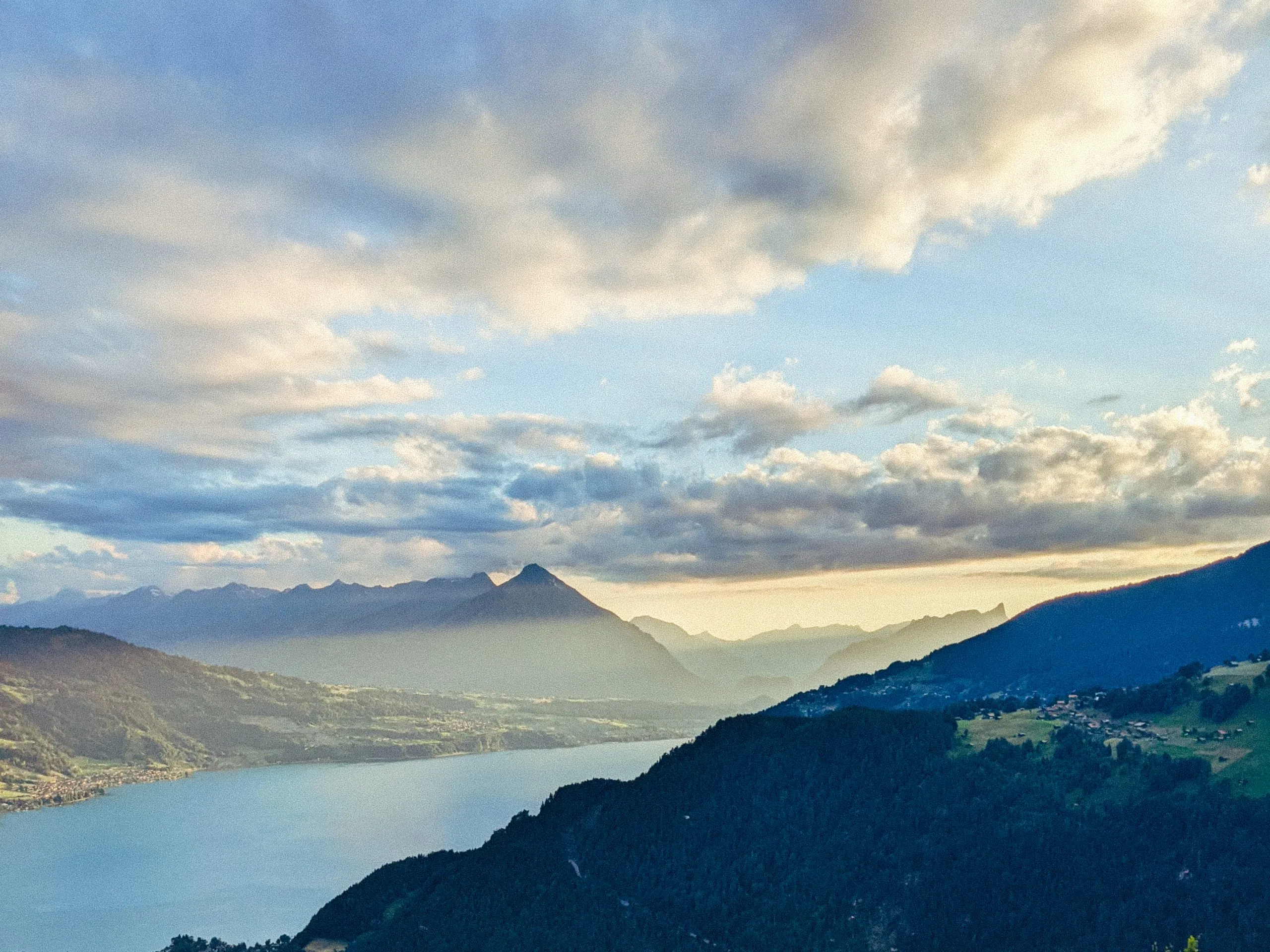 A lake and mountains under a soft evening sky, seen from a hillside