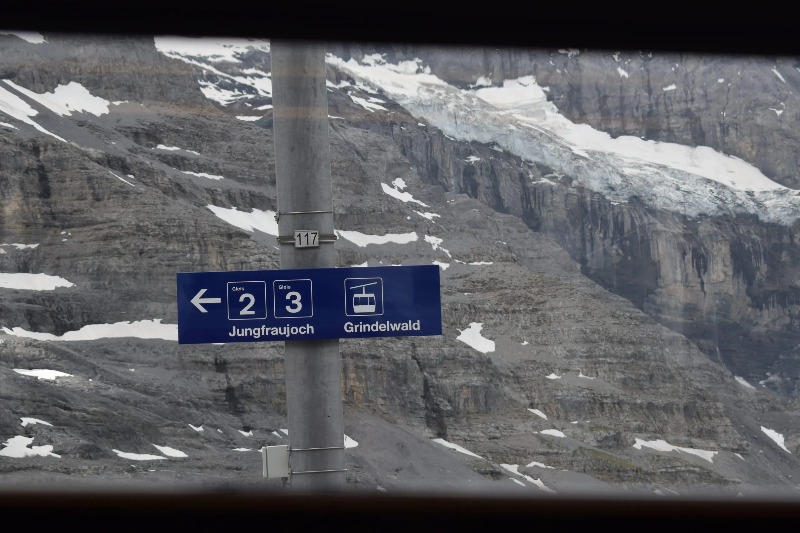 A station sign pointing to Jungfraujoch and Grindelwald in front of a snowy rock face