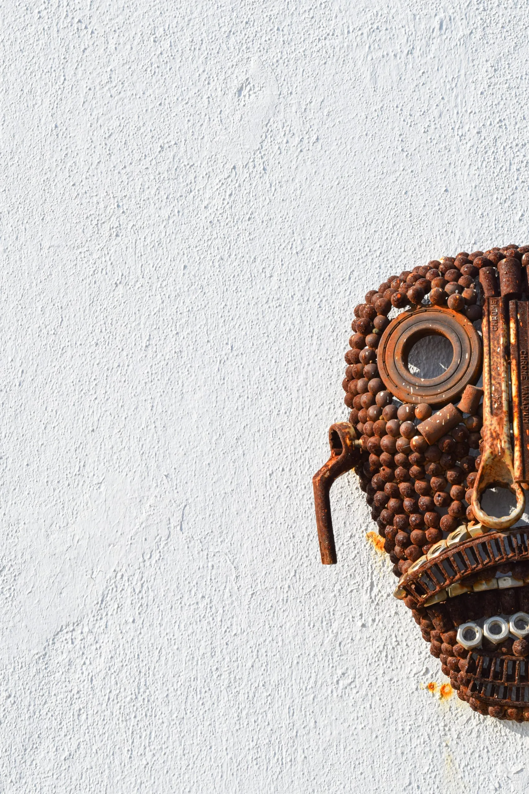 A rusty metal mask made of small round parts, cut off by the edge of a white wall